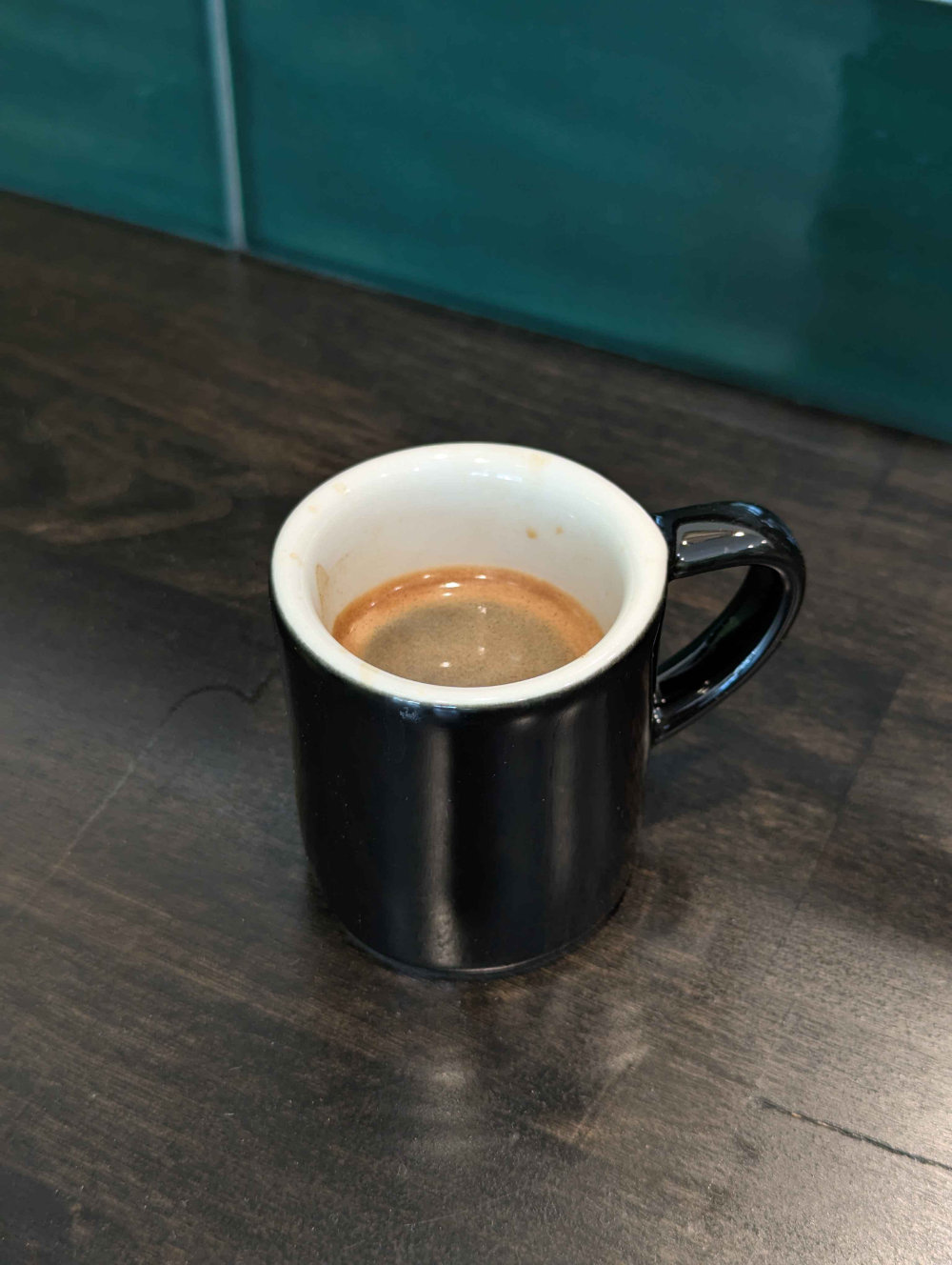 Photo of a shot-sized mug on a dark brown counter containing espresso.
