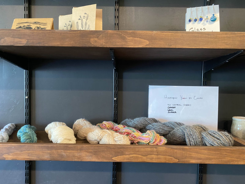 Zoomed in photo of a portion of the wooden merchandise shelf. Showcases various handspun yarns in different materials and colors.