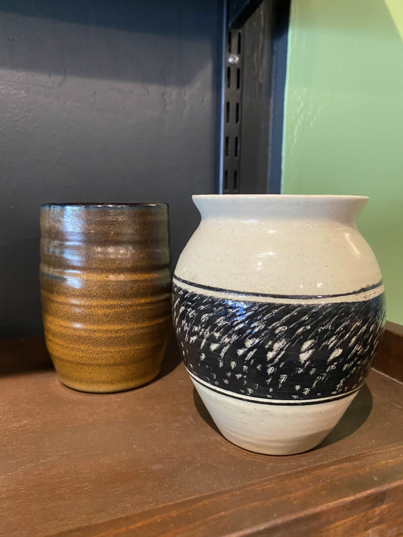 Zoomed in photo of a portion of the wooden merchandise shelf. Showcases handmade pottery, specifically two medium sized plant pots.
